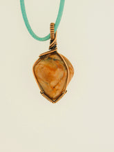 Load image into Gallery viewer, The #159 Feldspar Point from Copper Den Stone Jewelry features a polished orange gemstone, similar to aventurescent feldspar, elegantly wire-wrapped in oxidized copper and suspended from a teal cord.