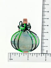 Load image into Gallery viewer, The #224 Green Aventurine Pumpkin pendant from Copper Den Stone Jewelry exhibits nature-inspired elegance with its translucent green aventurine and intricate black wire wrapping. This oval-shaped pendant, standing at approximately 1.5 inches tall, is elegantly displayed against a white backdrop with a black measurement scale on two sides, emphasizing its detailed design.
