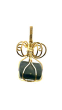 Load image into Gallery viewer, The #225 Shungite in Brass pendant from Copper Den Stone Jewelry features a large, dark green Shungite stone renowned for its EMF protection, elegantly encased in gold wire. Intricate swirled patterns above the stone lend an exquisite handcrafted appearance against a plain white background.