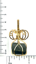 Load image into Gallery viewer, The #225 Shungite in Brass pendant from Copper Den Stone Jewelry showcases a dark stone wrapped in elegant brass wire. The design includes intricate loops and a top bail for easy attachment, positioned beside a ruler for scale. This piece not only provides EMF protection but also promotes emotional balance.