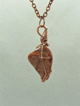 Load image into Gallery viewer, The #159 Feldspar Point, an exquisite pendant from Copper Den Stone Jewelry, showcases a polished brown stone beautifully wrapped in oxidized copper wire to enhance its natural allure. Known for its connection to abundance and manifestation, this remarkable piece elegantly hangs from a chain against a subtly textured light background.